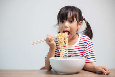 Cute Asian child girl eating delicious instant noodles at home.の写真素材