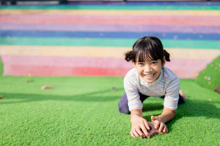 Cute Asian girl having fun trying to climb on artificial boulders at schoolyard playground, Little girl climbing up the rock wall, Hand Eye Coordination, Skills developmentの写真素材