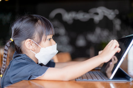 Happy Asian Child girl looks at tablet on the tableの写真素材