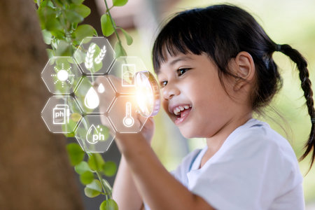 Asian little girl is looking at tree leaves through magnifier, outdoor shootの写真素材