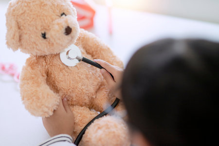 Asian girl playing with her patient plush bear in a doctor game, using a stethoscope. Children want to be a pediatrician doctorの写真素材