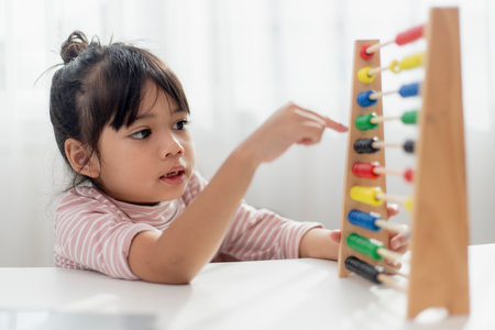 A young cute Asian girl is using the abacus with colored beads to learn how to count at homeの写真素材