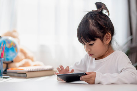 Asian kid girl having fun at home, using smartphone and laughing, playing video games on a mobile phone. kids and gadgets conceptの写真素材