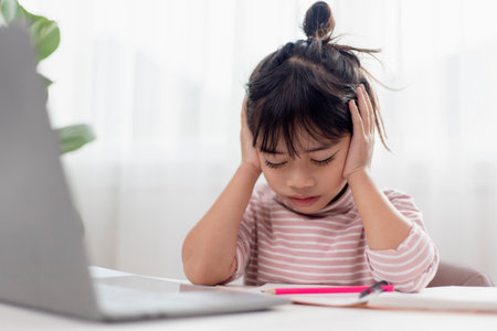 Little Asian girl sitting alone and looking out with a bored face, Preschool child laying head down on the table with sad bored with homework, spoiled childの写真素材