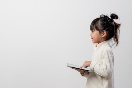 Asian little girl holding and using the digital tablet on white studio background, free copy spaceの写真素材