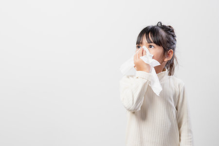 Asian child girl sick with sneezing on the nose and cold cough on tissue paper because weak or virus and bacteria from dust weatherの写真素材