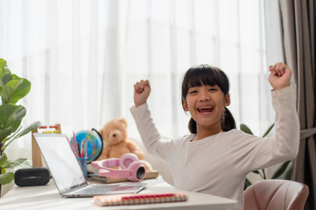 Asian schoolgirl doing her homework with laptop at home. Children use gadgets to study. Education and distance learning for kids. Homeschooling during quarantine. Stay at homeの写真素材