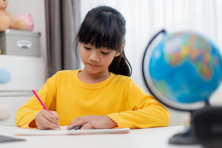 Asian schoolgirl doing her homework with digital tablet at home. Children use gadgets to study. Education and distance learning for kids. Homeschooling during quarantine. Stay at homeの写真素材