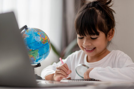 Asian schoolgirl doing her homework with laptop at home. Children use gadgets to study. Education and distance learning for kids. Homeschooling during quarantine. Stay at homeの写真素材