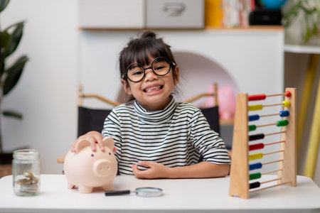 Little Asian girl saving money in a piggy bank, learning about saving, Kid save money for future education. Money, finances, insurance, and people conceptの写真素材
