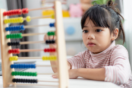 A young cute Asian girl is using the abacus with colored beads to learn how to count at homeの写真素材