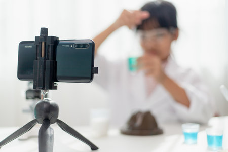 Asian school girl making easy chemistry experiments and recording a video for his followers, Young blogger kid posing in front of camera for vlog, Children make vlog for social media channel concept.の写真素材