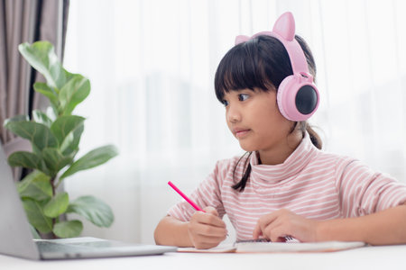 Asian little girl in headphones have video call distant class with teacher using laptop, study online on computer, homeschooling conceptの写真素材