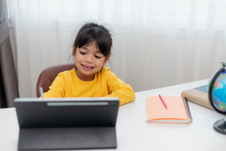 Asian schoolgirl doing her homework with digital tablet at home. Children use gadgets to study....