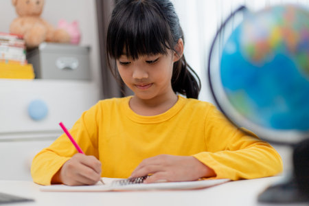 Asian schoolgirl doing her homework with digital tablet at home. Children use gadgets to study. Education and distance learning for kids. Homeschooling during quarantine. Stay at homeの写真素材