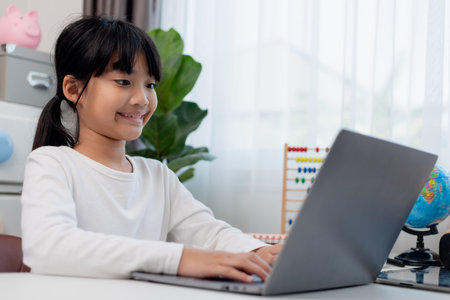 Asian schoolgirl doing her homework with laptop at home. Children use gadgets to study. Education...