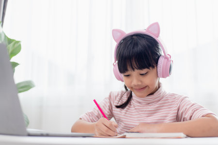 Asian little girl in headphones have video call distant class with teacher using laptop, study online on computer, homeschooling conceptの写真素材