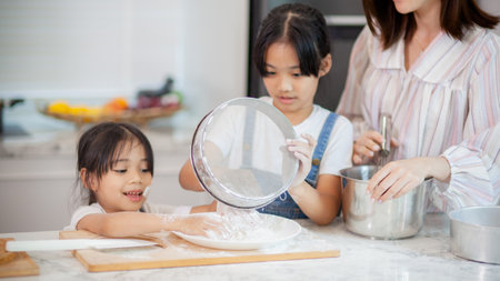 Two little cute Asian girls, learning how to make bread and bakery with a curious and happy smile face. She learns and playsの写真素材