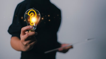 à¹Hand holding light bulb with question mark icon on a dark background, problem solving, searching for answers.の写真素材