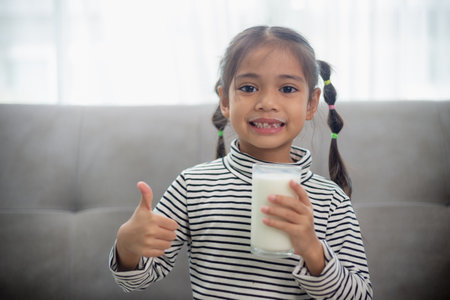 Asian little cute kid holding a cup of milk in the house. feel happy and enjoy drinking milk.の写真素材