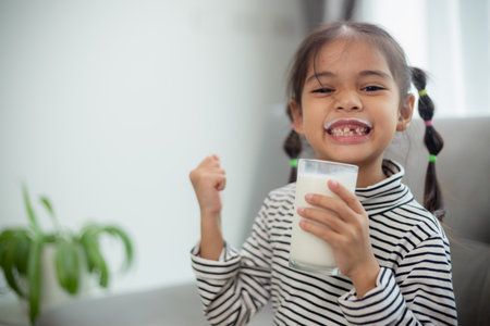 Asian little cute kid holding a cup of milk in the house. feel happy and enjoy drinking milk.の写真素材