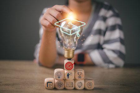 Hands-touching light bulb with graduation hat on wooden cubes stacked, Internet education course degree, E-learning graduate certificate program concept. study knowledge to creative thinking ideas.の写真素材