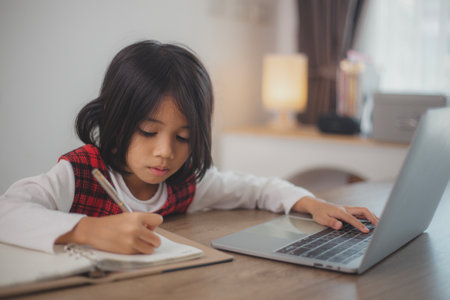 Cute and happy little Asian girl children using a laptop computer, studying through an online e-learning system at home.の写真素材