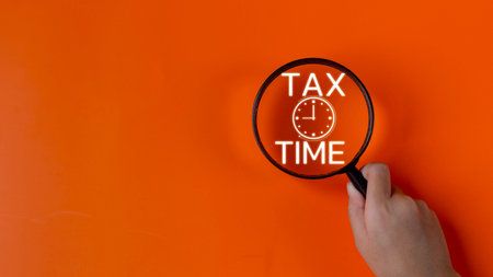Hand holding a Magnifier glass with the word tax times an alarm clock. Tax payment reminder or...