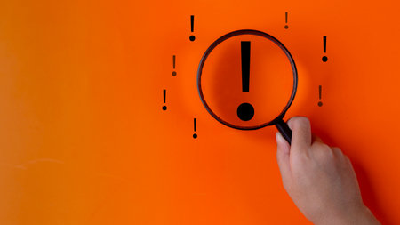 Magnifying glass focuses on an Exclamation mark icon over the orange background with copy space for...