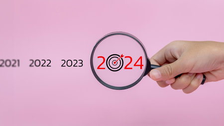 Target of business concept. Hand-holding magnifier focusing on the year 2024. Focus on new business goals, plans, and strategies of the year 2024 concept.の写真素材