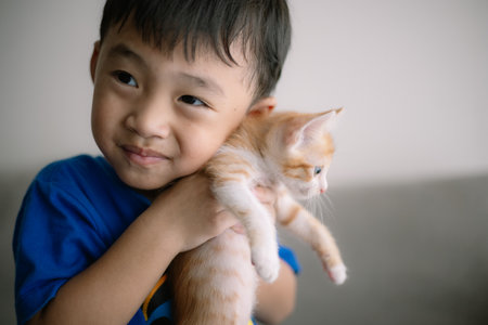 A young boy is holding a kitten in his arms. The boy is smiling and he is happyの写真素材