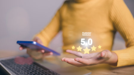 A woman is holding a cell phone and a laptop, with a 5 star rating on the phoneの写真素材
