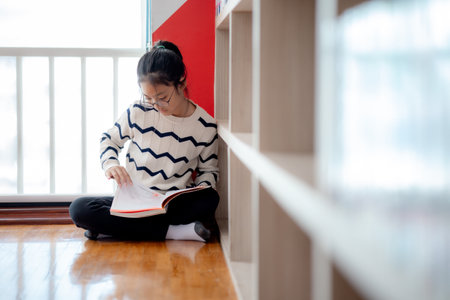 A girl is sitting on the floor reading a book. She is wearing glasses and a striped sweaterの写真素材