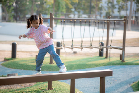 A little girl is playing on a park equipment. She is wearing a pink shirt and blue jeans