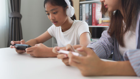 Asian kids play online video games with friends on mobile phones for fun at home.