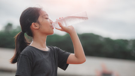 A girl drinking water from a bottle. The girl is wearing a black shirt and has her hair in a...