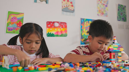 Two children are playing with legos in a room with colorful pictures on the wall. Scene is playful...