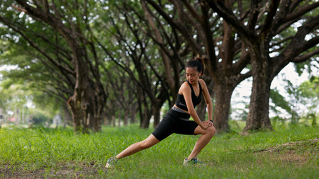 A woman is stretching her leg on a sidewalk next to a pole. The pole is near a road and there are...