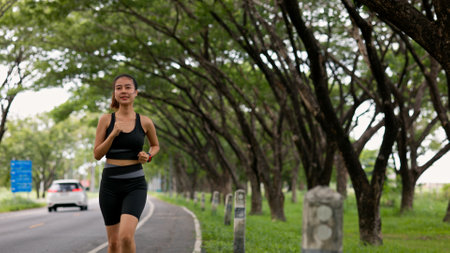 A woman runs down a road next to a car. The road is lined with trees and the woman is wearing a black tank topの写真素材