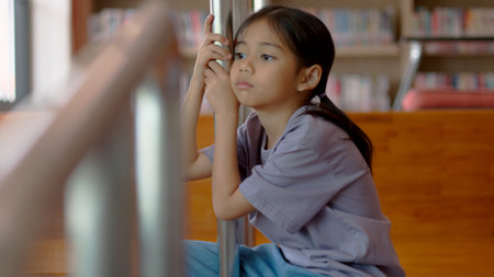 An Asian girl sits on the stairs with a bored expression on her face. Her dim eyes reflect her disinterest in her surroundings.の写真素材