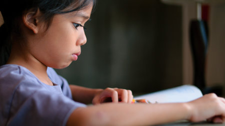 An Asian girl is reading a book in a library, looking serious as she focuses on the contents.の写真素材