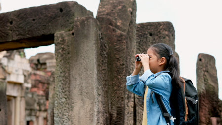 An Asian woman explores an ancient stone temple using binoculars to admire its stunning architecture.の写真素材