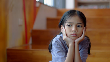 An Asian girl sits on the stairs with a bored expression on her face. Her dim eyes reflect her disinterest in her surroundings.の写真素材