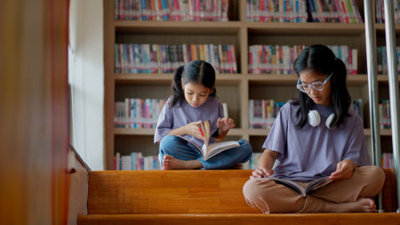 Two Asian siblings sit on the steps of a library, intently reading a book together, and share a moment of discovery and curiosity.の写真素材