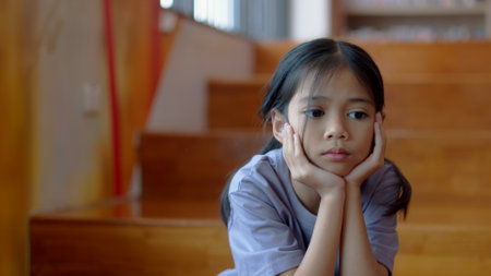 An Asian girl sits on the stairs with a bored expression on her face. Her dim eyes reflect her disinterest in her surroundings.の写真素材
