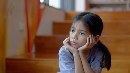 An Asian girl sits on the stairs with a bored expression on her face. Her dim eyes reflect her disinterest in her surroundings.の写真素材
