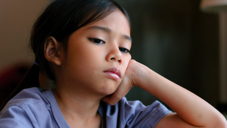 An Asian girl sits at a table in a library, her face clearly showing boredom as she looks away from the open book in front of her. She looks disinterested and lost in thought.の写真素材