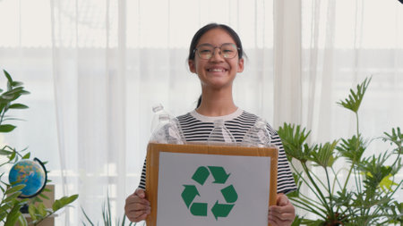 A cute Asian girl carries a paper box full of plastic water bottles. Children sort out trash for recycling. Cultivate the learning of waste separation. The child smiles sweet and brightの写真素材