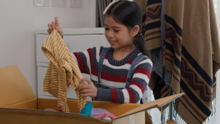 Asian little girls sorting clothes and packing into box. Donations for charity, help low income families, declutter home, sell online, moving moving into new home, recycling, sustainable livingの写真素材