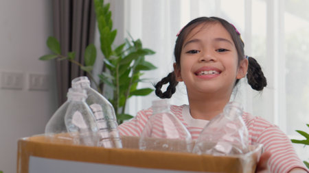 A cute Asian girl carries a paper box full of plastic water bottles. Children sort out trash for recycling. Cultivate the learning of waste separation. The child smiles sweet and brightの写真素材